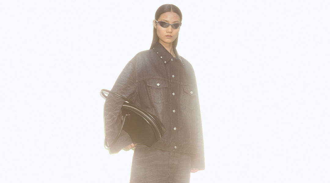 Acne Studios model wearing futuristic sunglasses, a denim-on-denim outfit and holding a sculptural black handbag