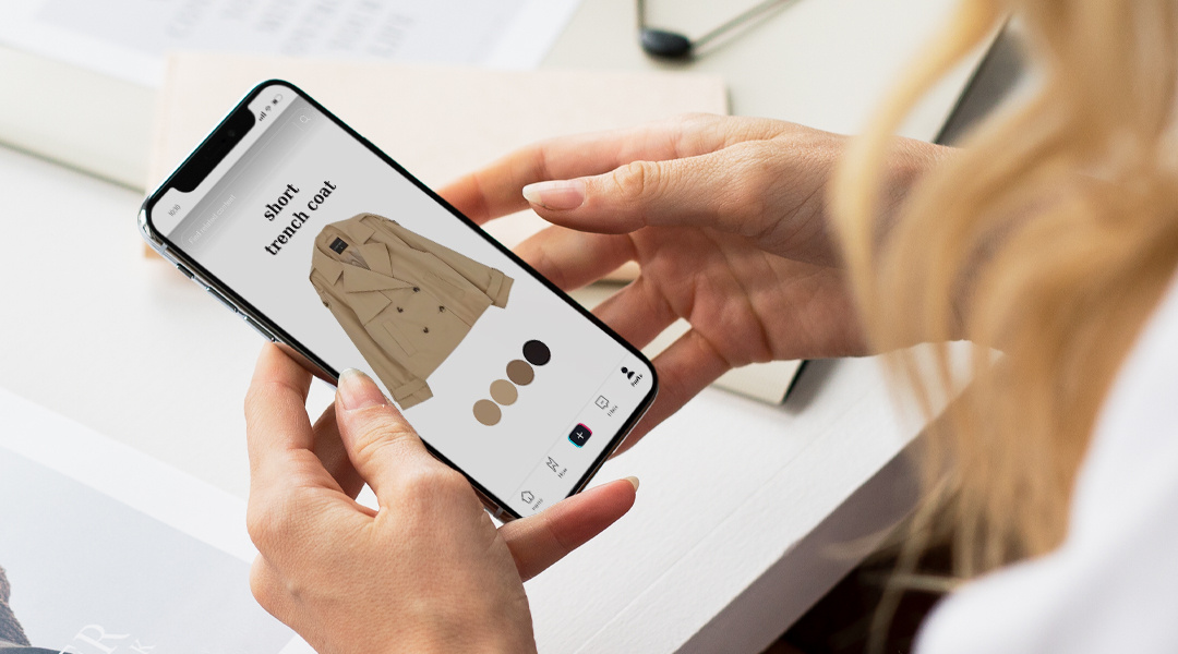 a consumer's hands holding a smartphone viewing a trench coat on an ecommerce site